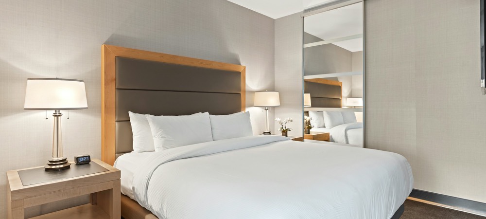 A hotel room with a king bed made up in white linen and pillows