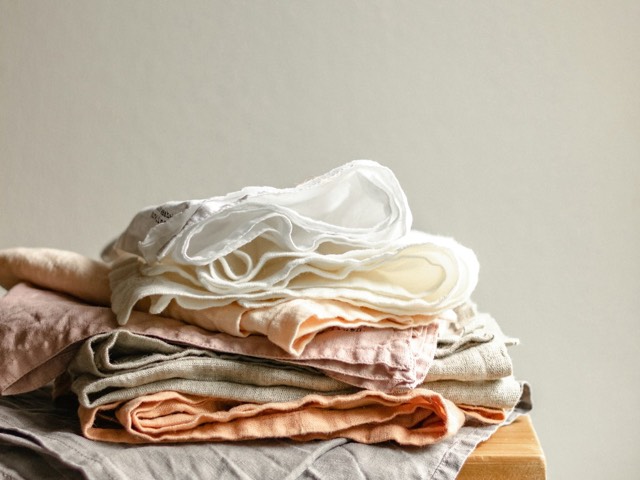 A neat stack of folded linens in white, blush and stone on a wooden stool